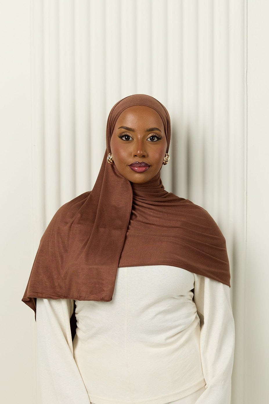 Person wearing a brown hijab and white outfit against a white background