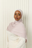 Woman wearing a light pink hijab and white outfit against a white background