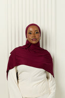 Person wearing a maroon hijab and white outfit against a white curtain background