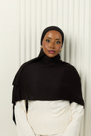 Woman wearing a black hijab and white outfit against a light background